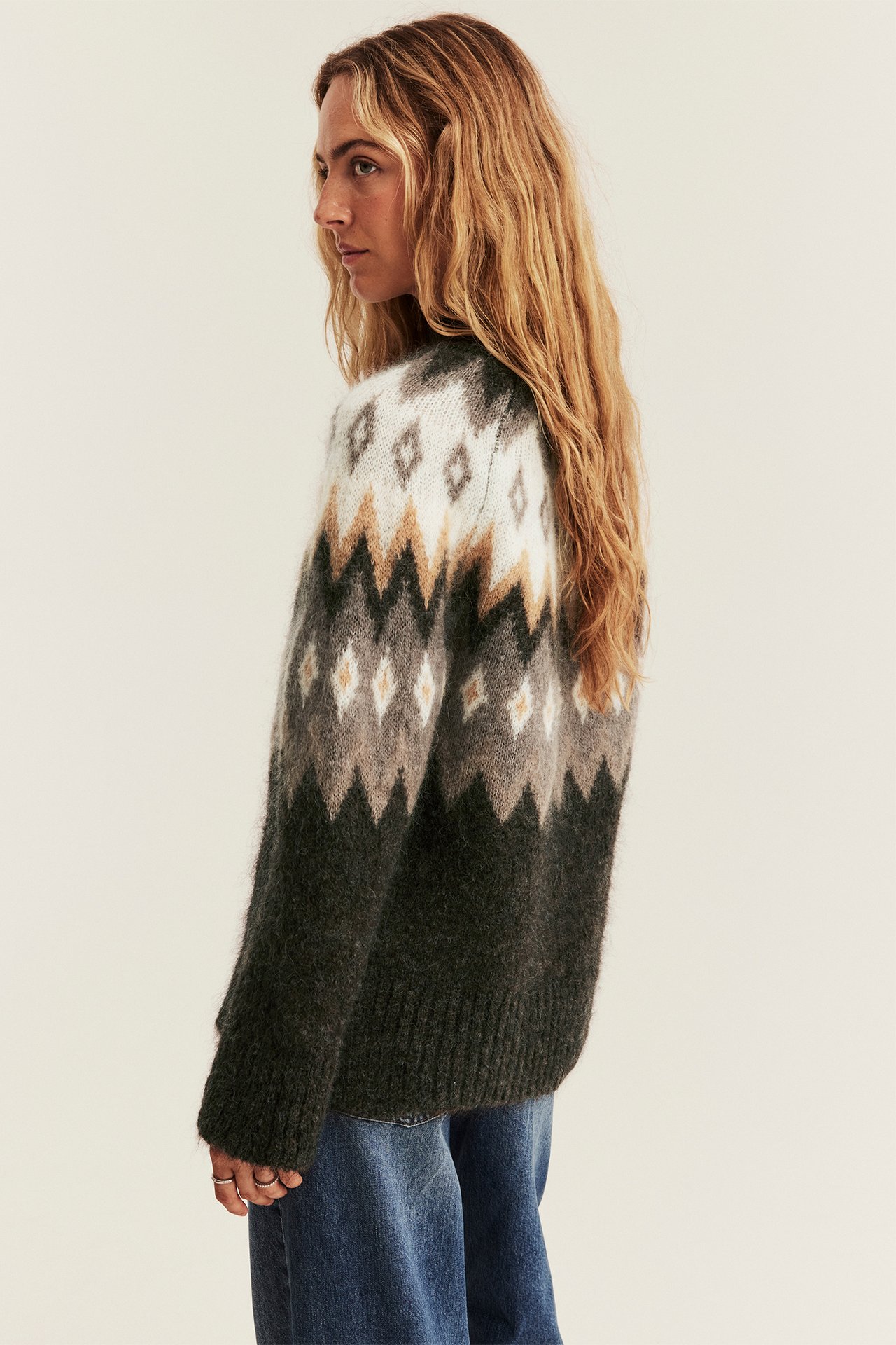 Seitenansicht Frau in dunkelgrünem gemustertem Fair Isle Pullover und blauen Jeans.