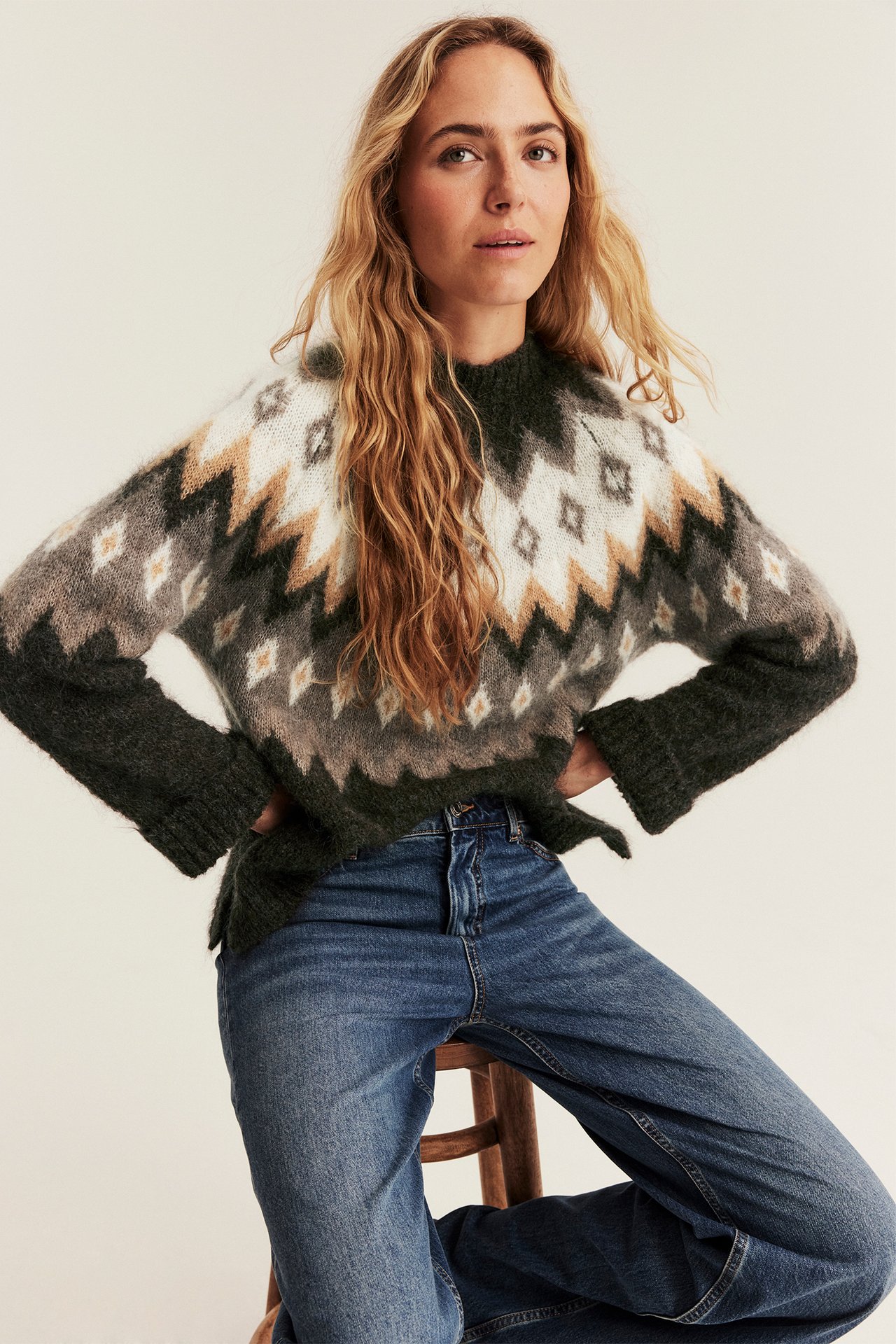 Weibliches Modell in fair isle Strickpullover (grün, weiß, beige, grau) und blauer Jeans.