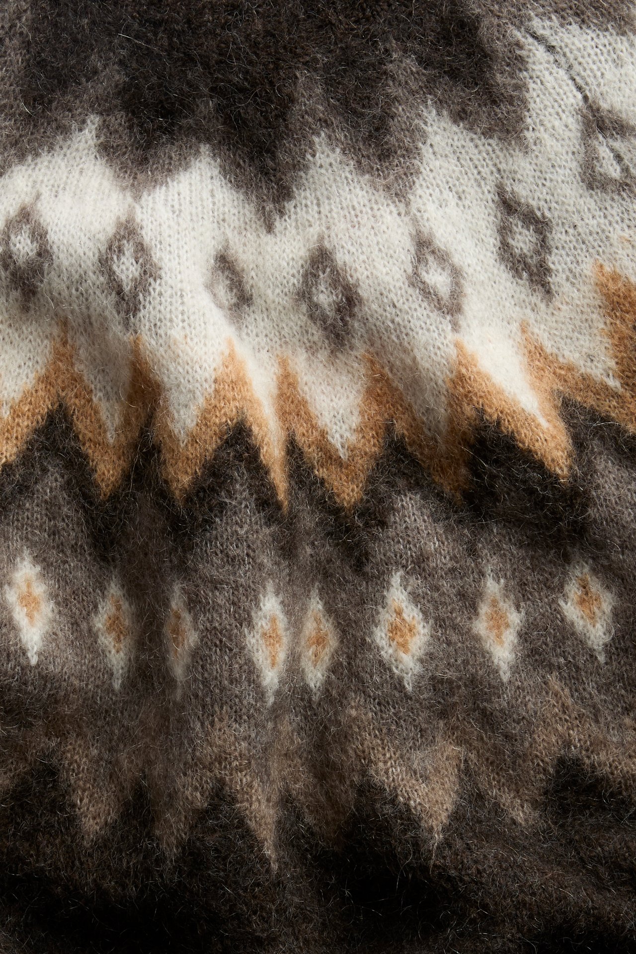 Nahaufnahme eines dunkelbraunen, weißen und hellbraunen gemusterten Strickpullovers.
