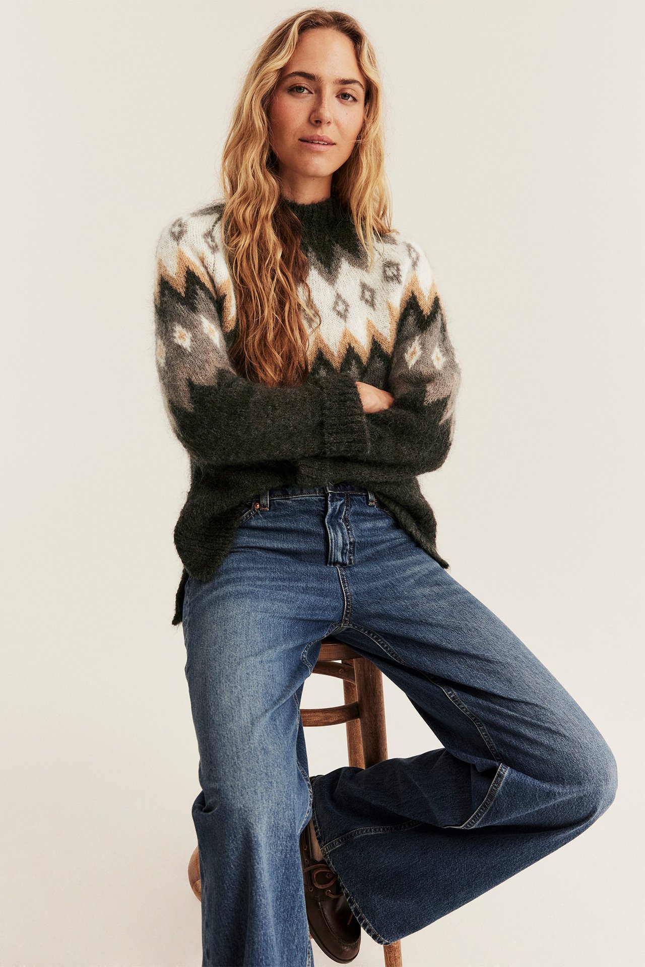 Vorderansicht: Frau in gemustertem Pullover, blauen weiten Jeans und dunkelbraunen Loafern.