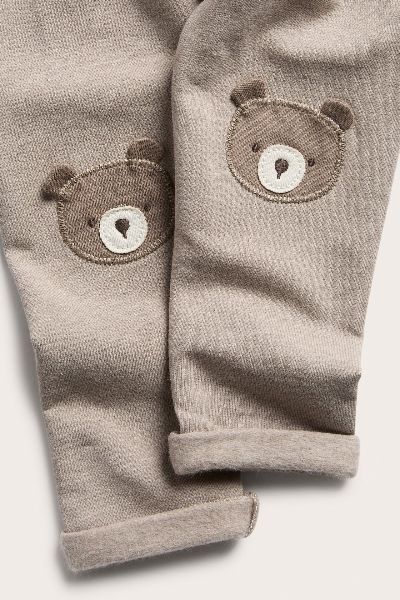 Close-up of light brown baby pants with brown bear knee patches and rolled cuffs.