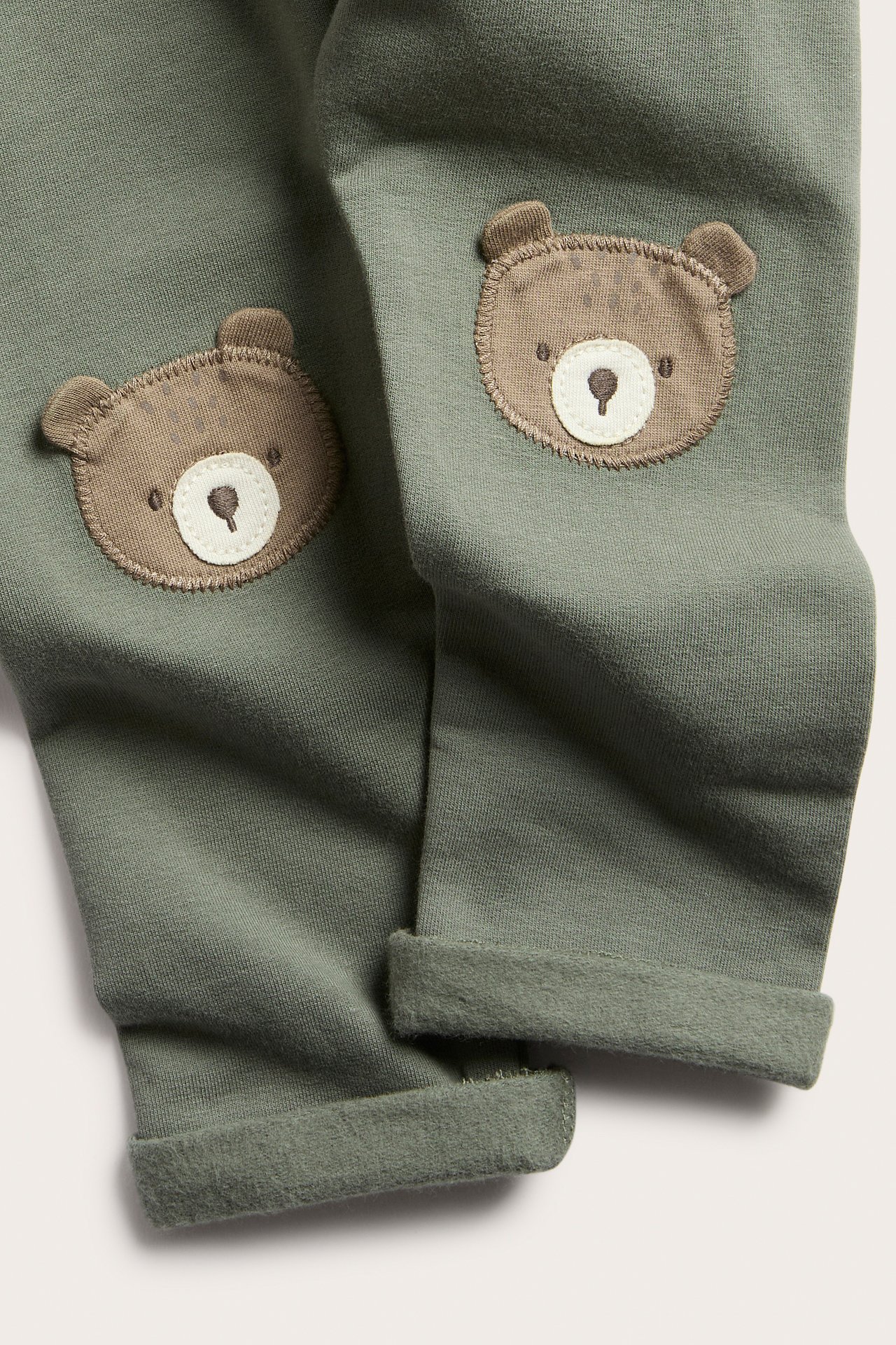 Close-up of green baby sweatpants with brown bear knee patches and rolled cuffs.