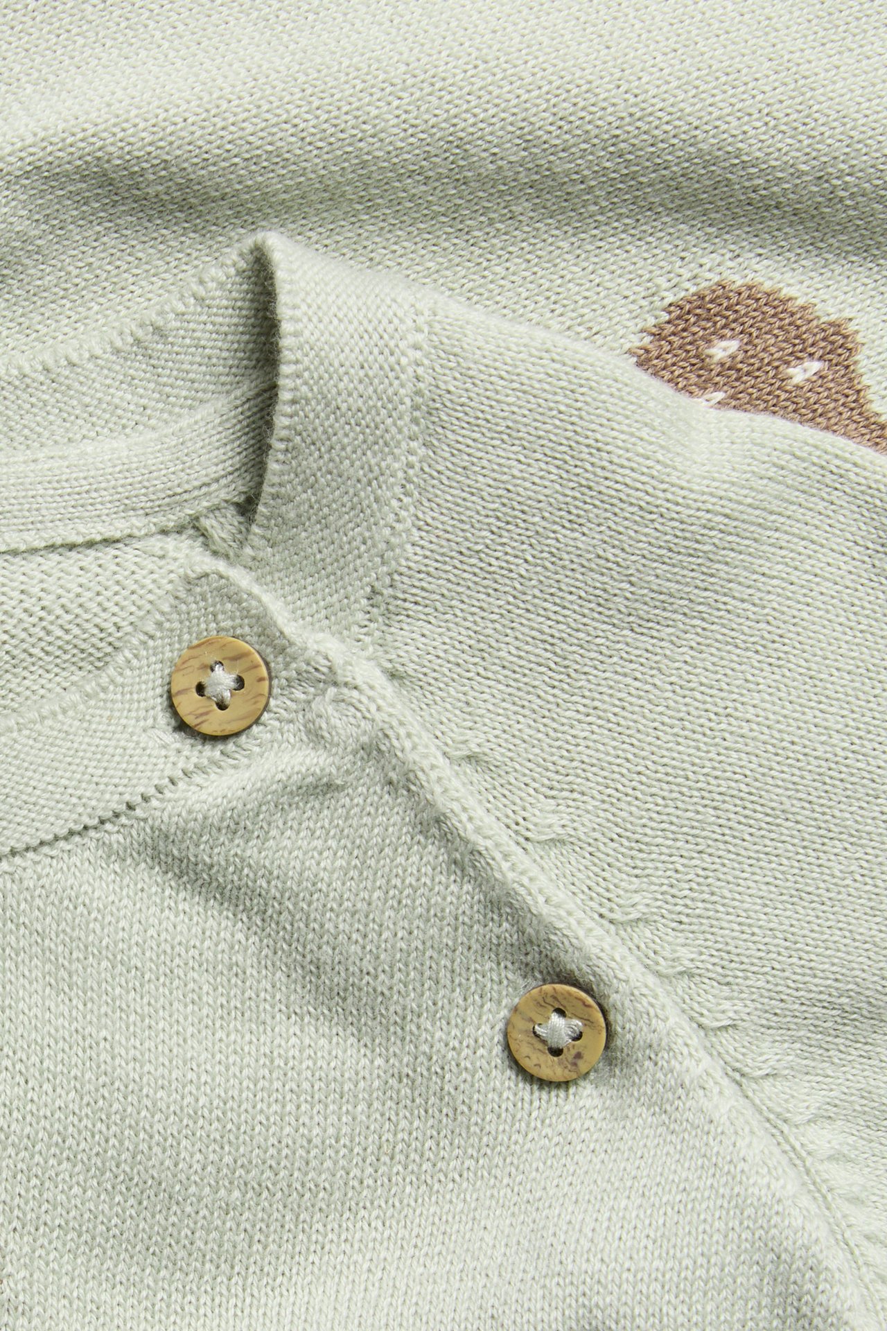 Nahaufnahme einer hellgrünen gestrickten Baby-Strickjacke mit Holzknöpfen und braunem Druck.