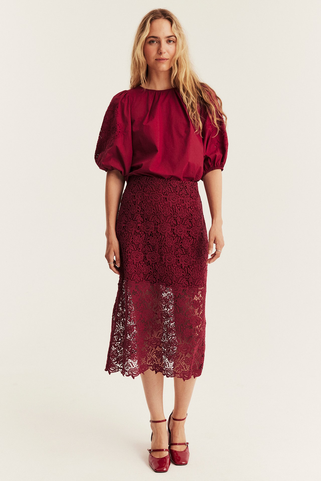 Front view, woman in burgundy lace midi skirt, puff sleeve blouse, and Mary Jane shoes.
