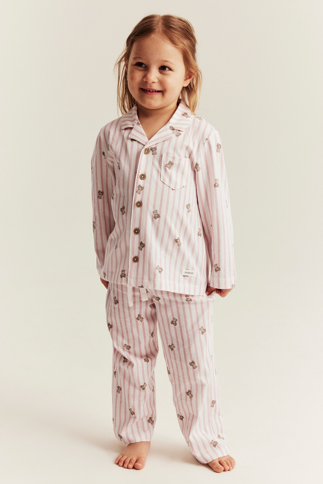 Front view of a kid wearing a light pink and white striped cotton pajama set with a teddy bear pattern.