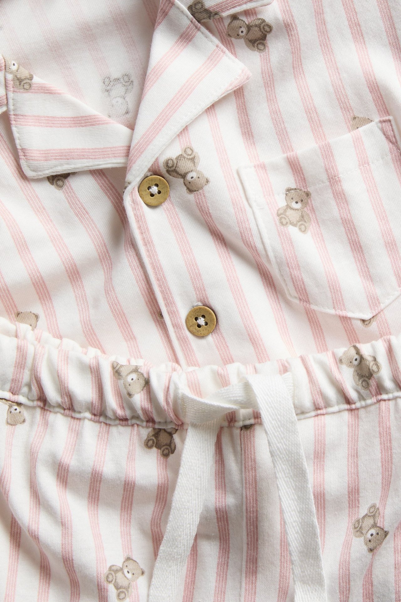 Close-up: Light pink striped cotton pyjama set with teddy bear print. Button-front top, drawstring waist bottoms.