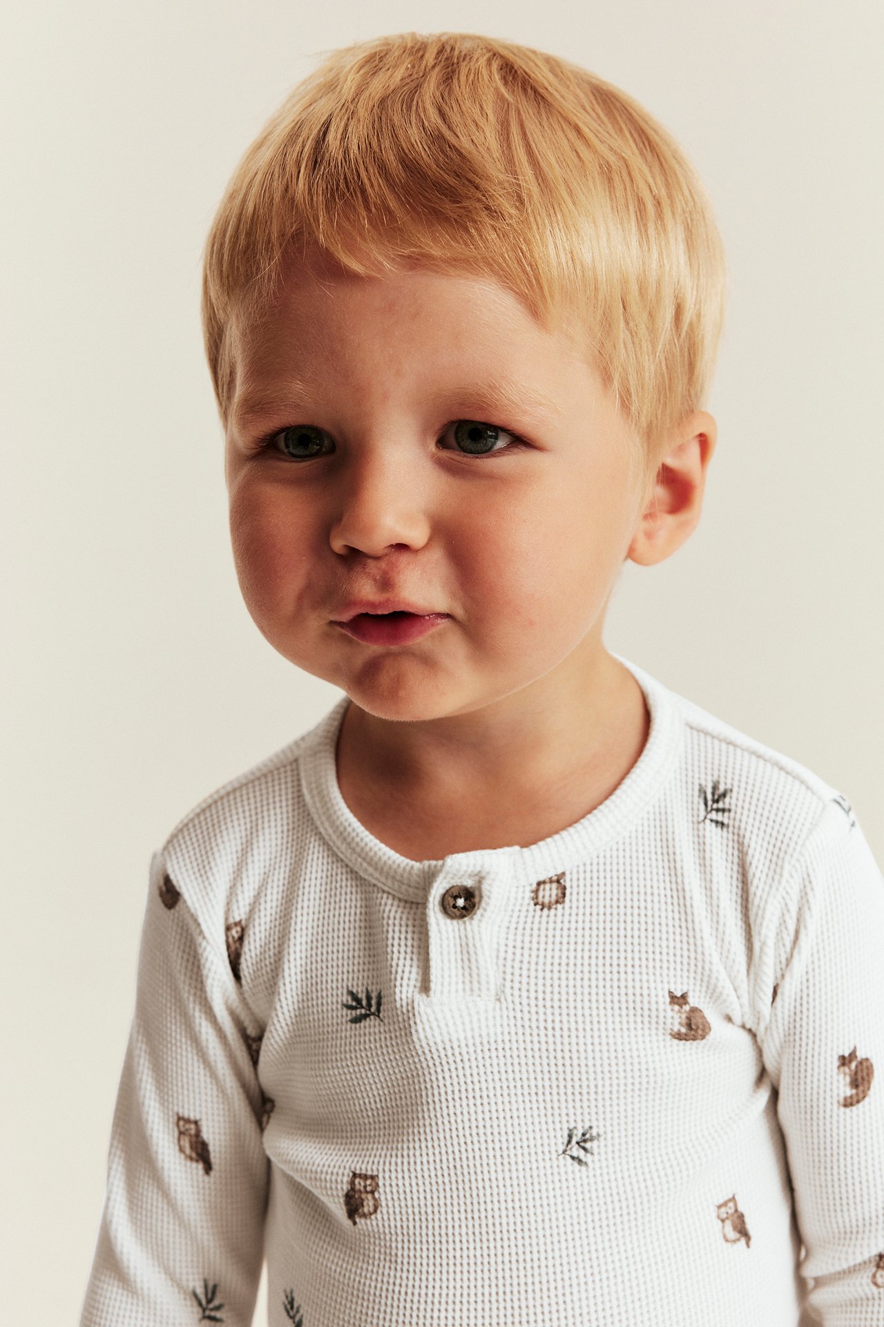 Close-up of a kid wearing a white waffle-knit long-sleeved top with animal print and two buttons.