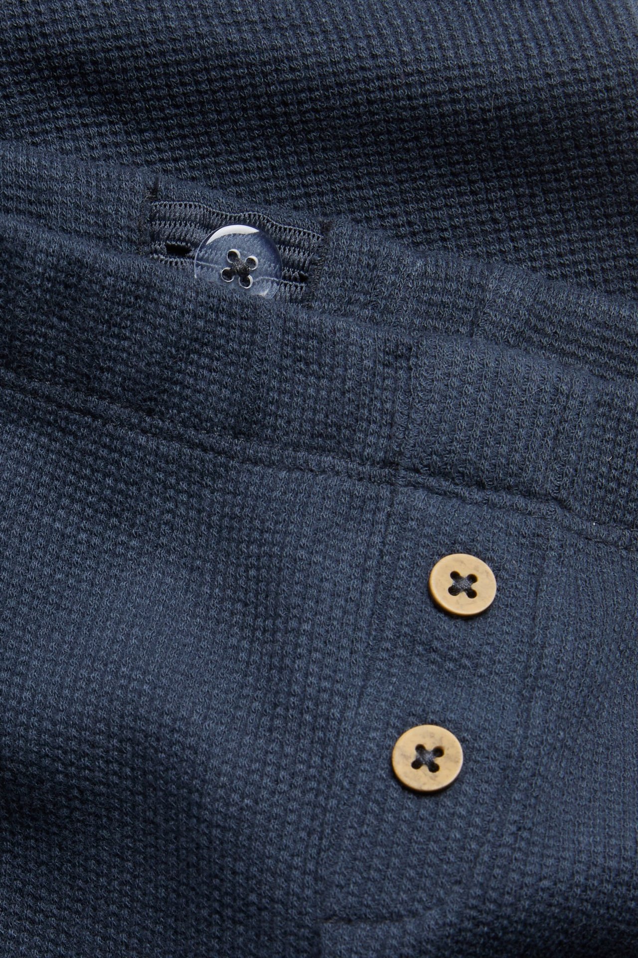 Close-up of a dark blue waffle-knit garment with a translucent and two wooden buttons.