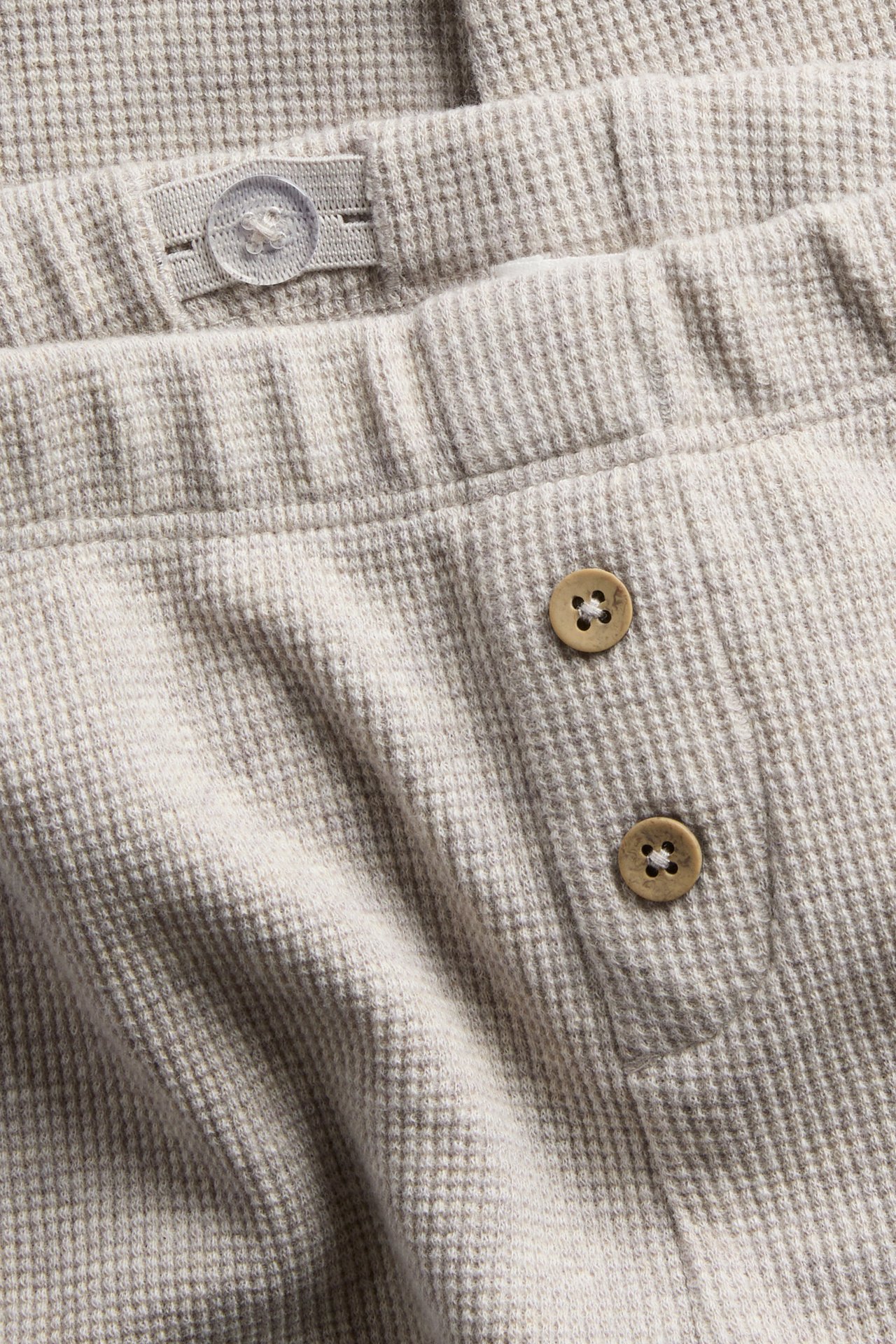 Close-up of a light beige waffle knit garment featuring an adjustable waist and two brown buttons.