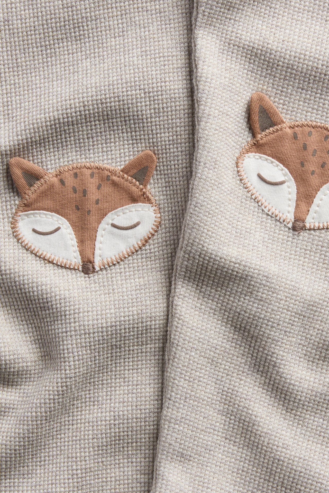 Close-up of a light beige waffle-knit fabric with two embroidered sleeping fox appliques.