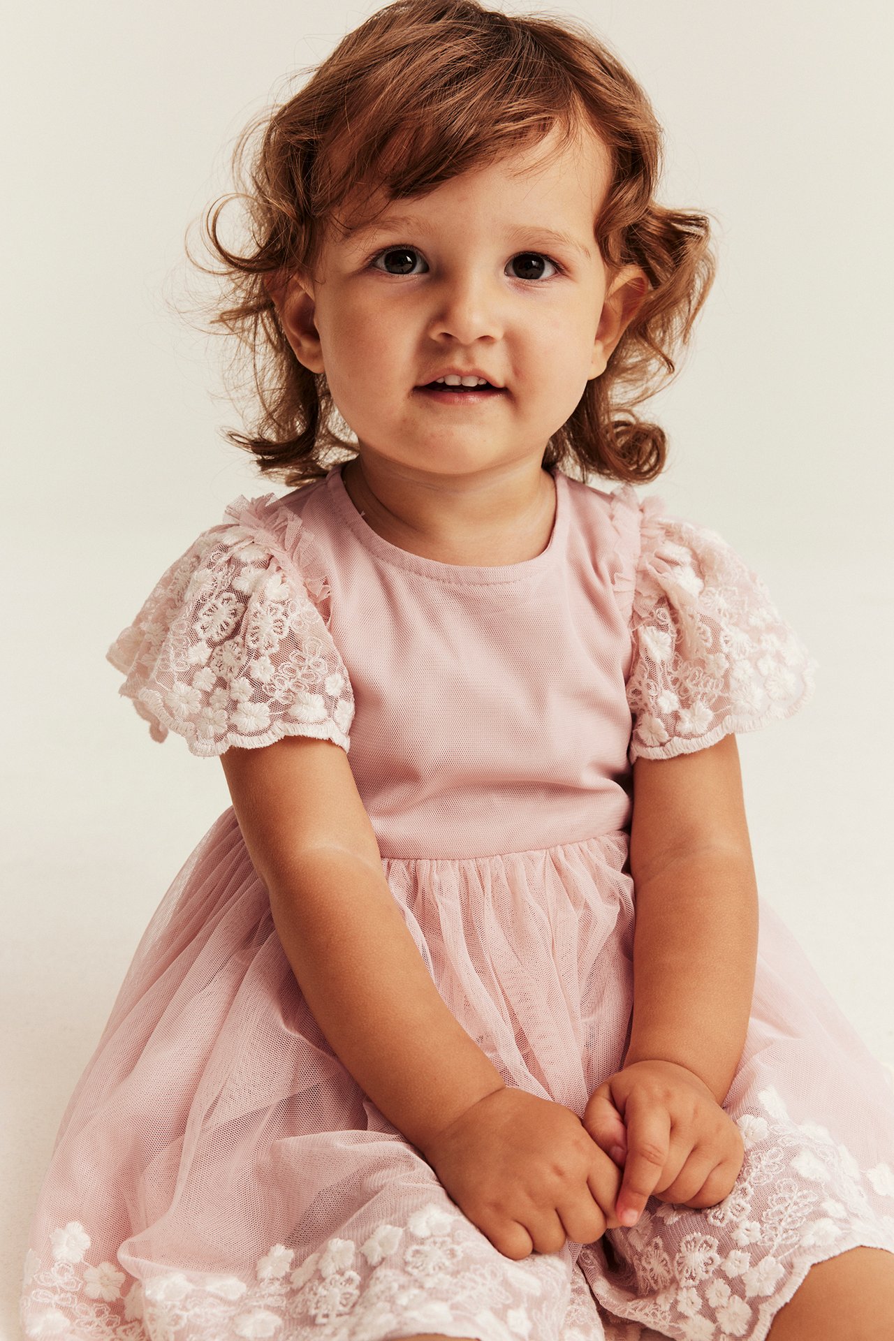Vorderansicht eines Baby-Mädchens in rosa Kleid mit Spitzenärmeln und besticktem Tüllrock.
