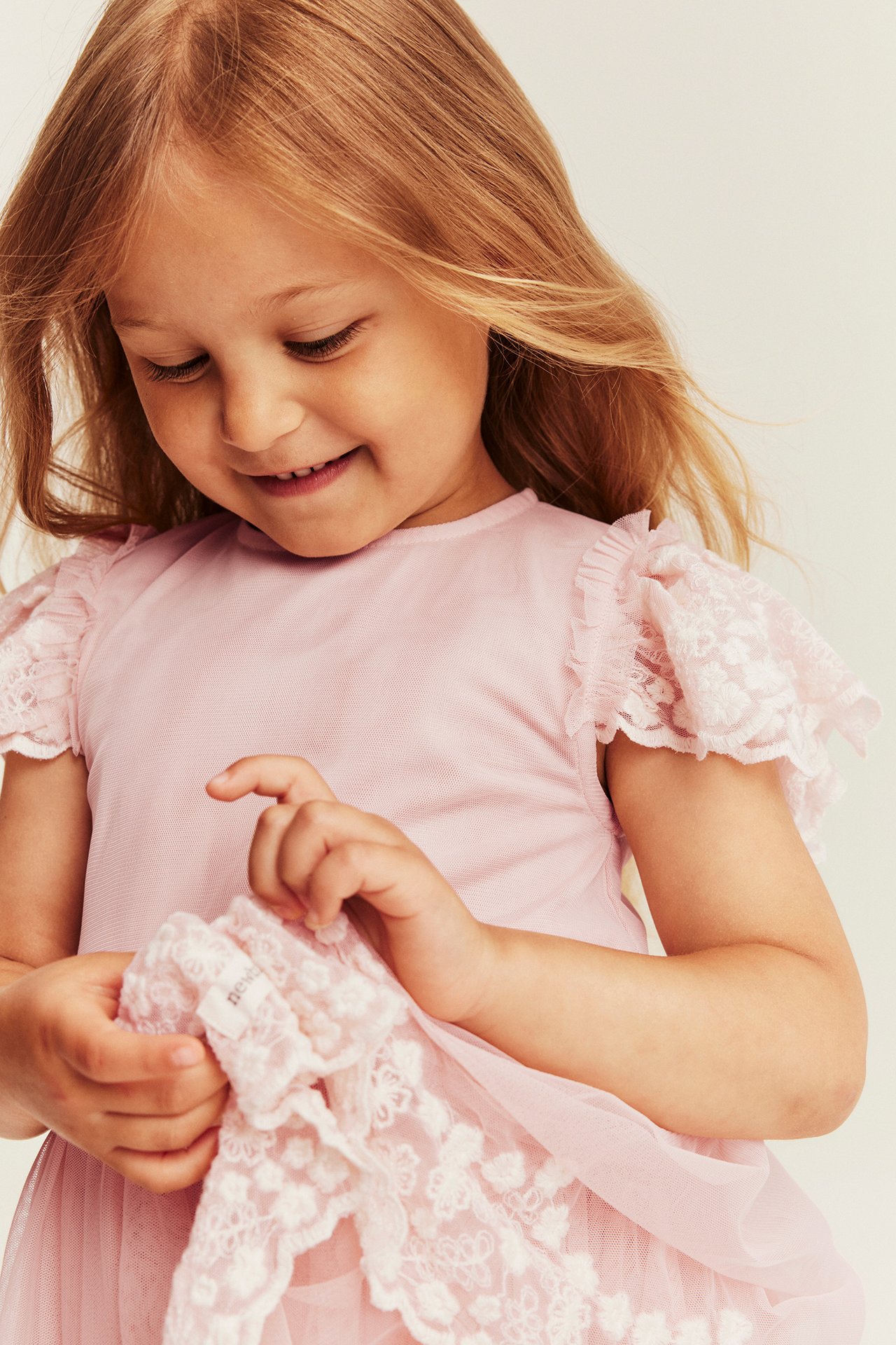 Close-up of a kid wearing a pink lace dress with ruffled sleeves, holding matching pink lace.