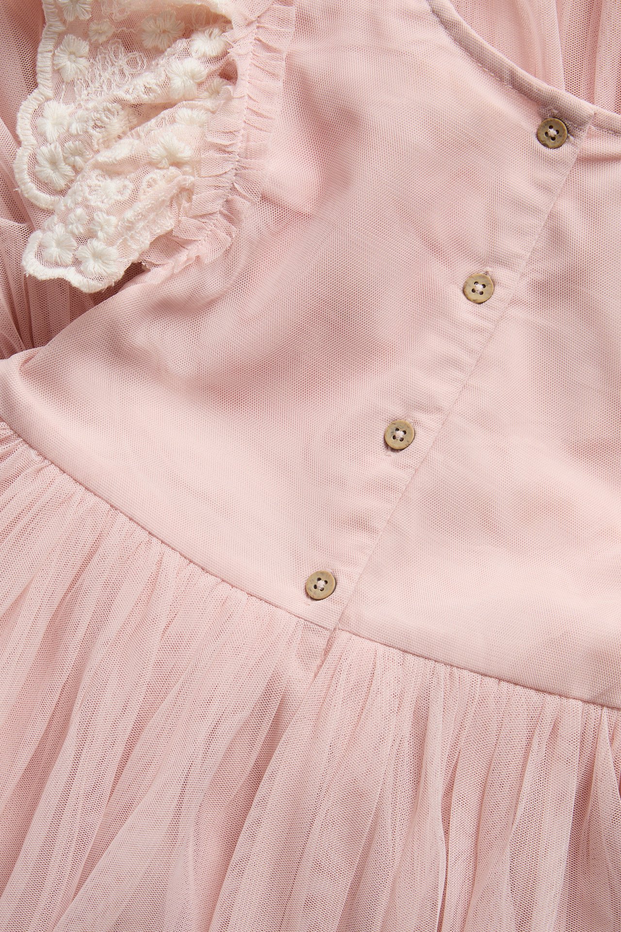 Close-up of a pink tulle and lace dress with a front button placket.