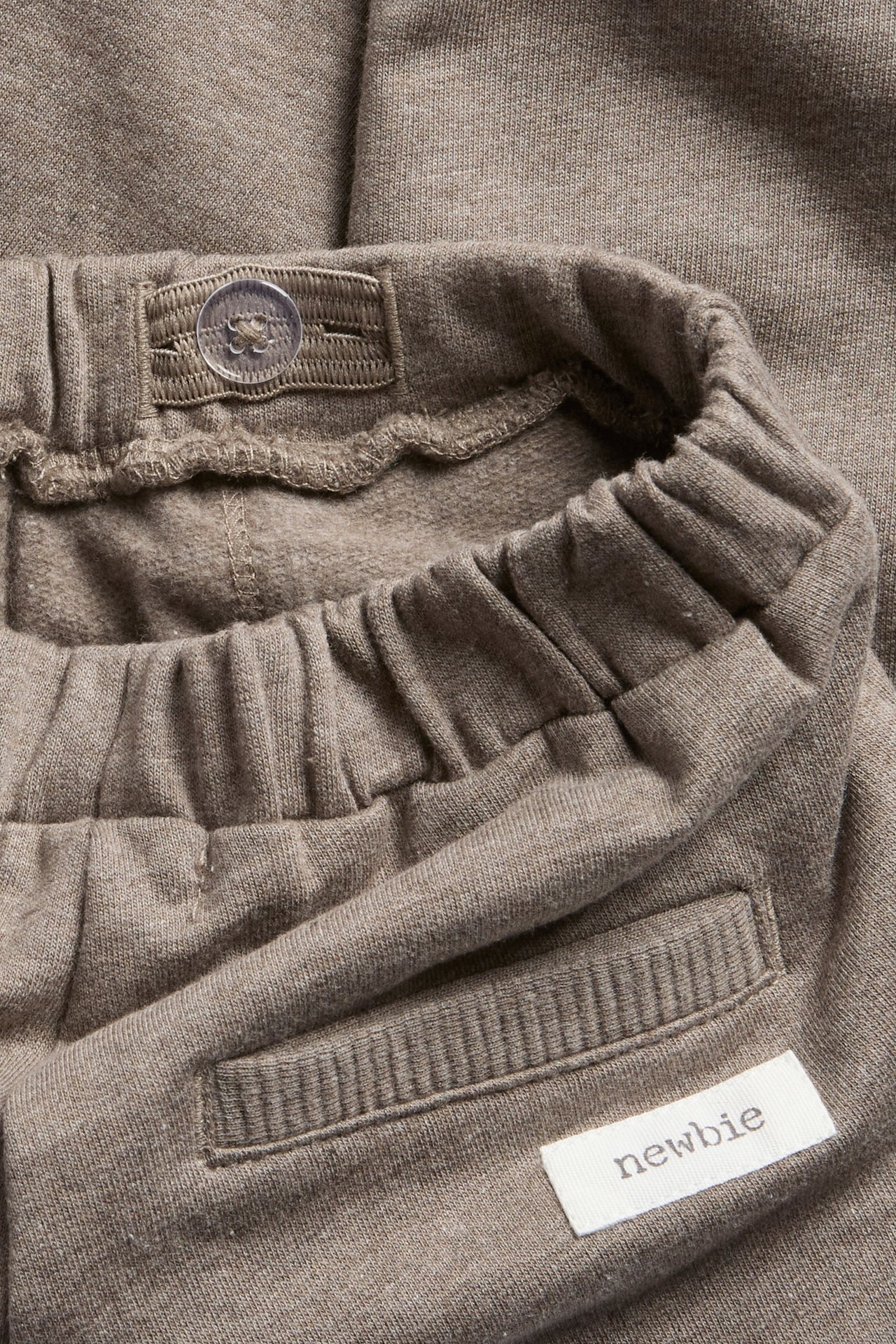 Close-up of brown baby sweatpants showing elastic waist with button and Newbie label.