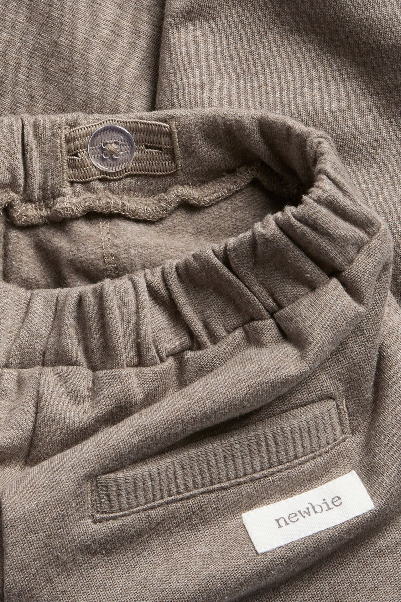 Nahaufnahme einer braunen Baby-Jogginghose mit elastischem Bund, Knopf und Newbie-Etikett.