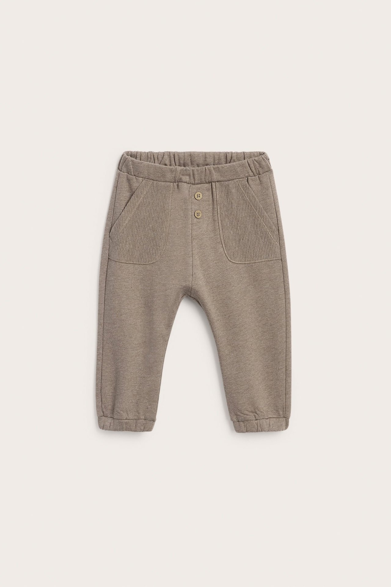 Vorderansicht: Taupefarbene Babyhose aus Jersey mit Gummizug, zwei Knöpfen und gerippten Taschen.
