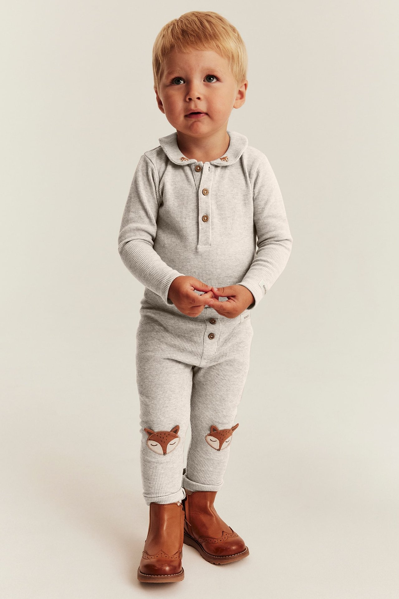 Front view of baby boy in light grey ribbed top and pants with fox knees, brown boots.