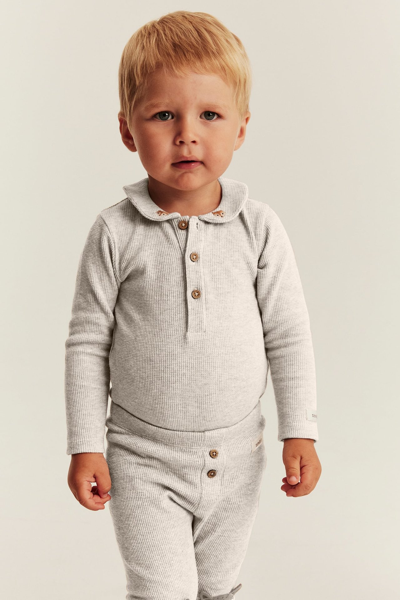 Front view of a baby wearing a light grey ribbed long-sleeved top with a collar and matching pants.