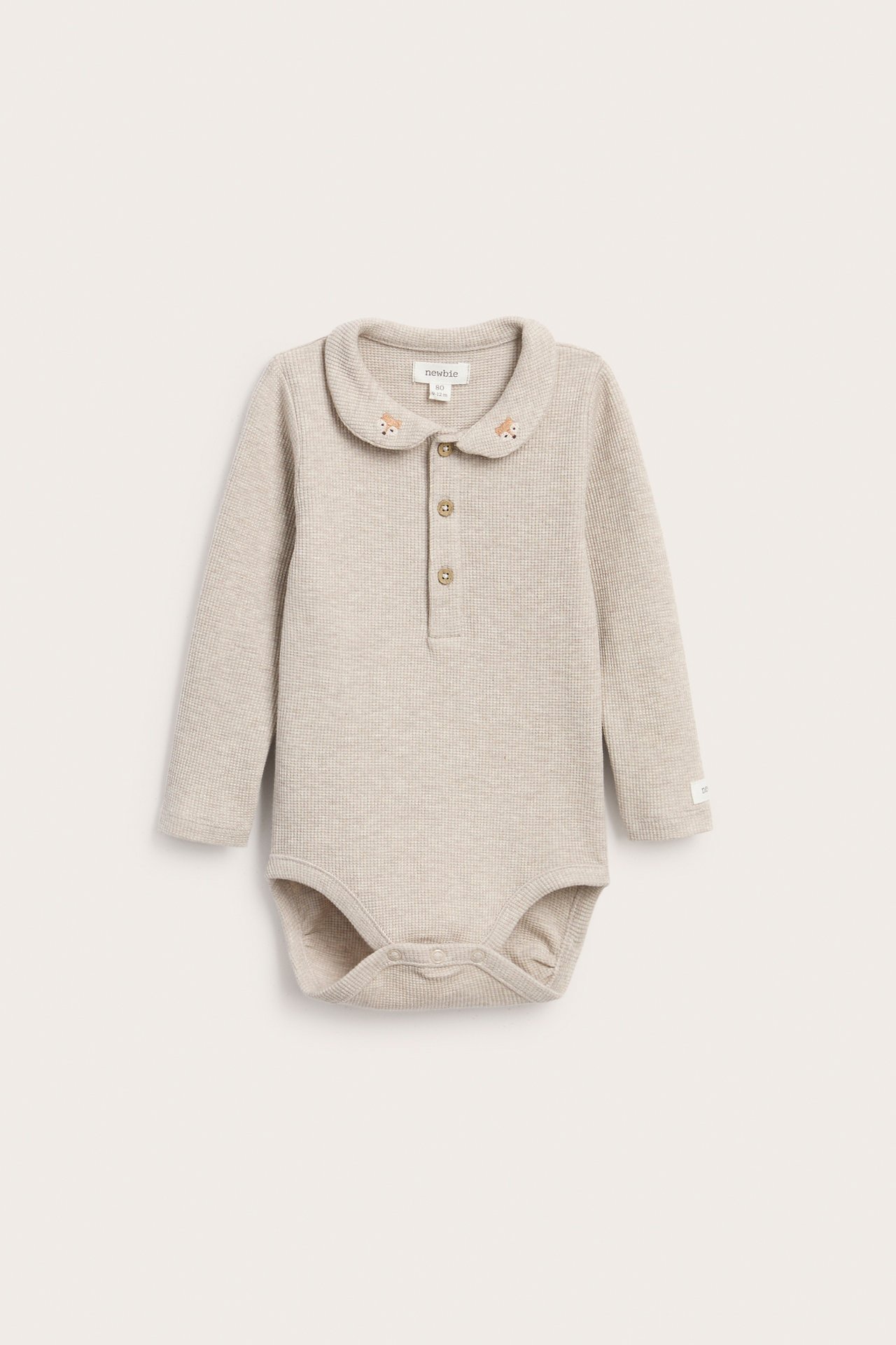 Vorderansicht eines beigen, gerippten Langarm-Babybodys mit besticktem Kragen und Knopfleiste.