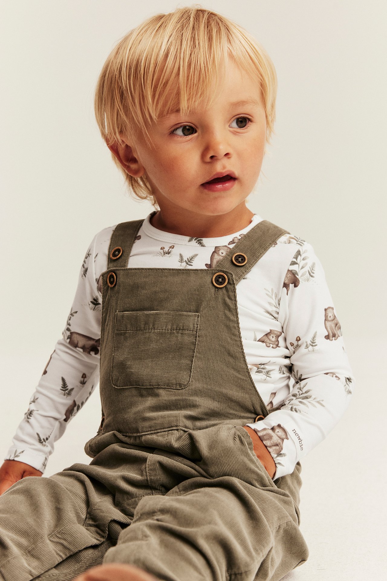 Kinder-Olivgrün-Cord-Overall über weißem Bären-Print-Langarmshirt.