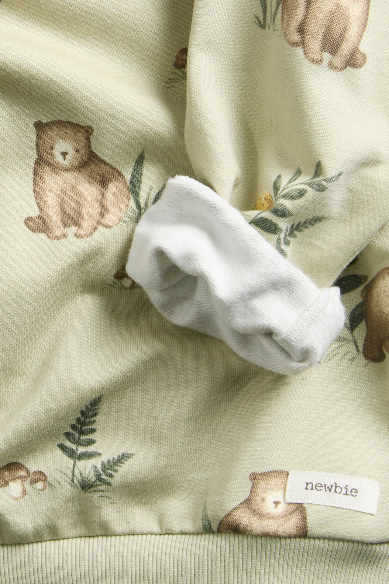 Close-up of a light green baby sweatshirt with a bear and forest print, showing a white cuff.