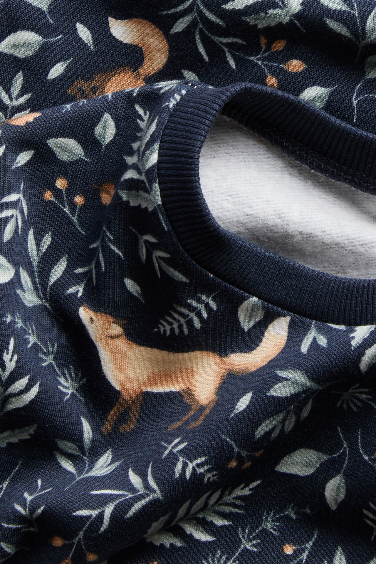 Nahaufnahme eines dunkelblauen Sweatshirts mit Fuchs- und Blätterdruck, das den gerippten Halsausschnitt zeigt.