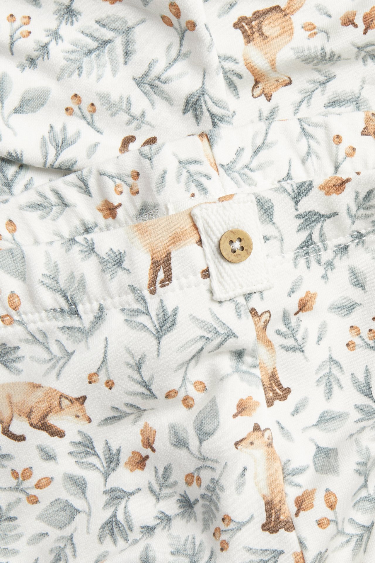 Close-up of white fabric with a fox and foliage print, featuring a brown wooden button.