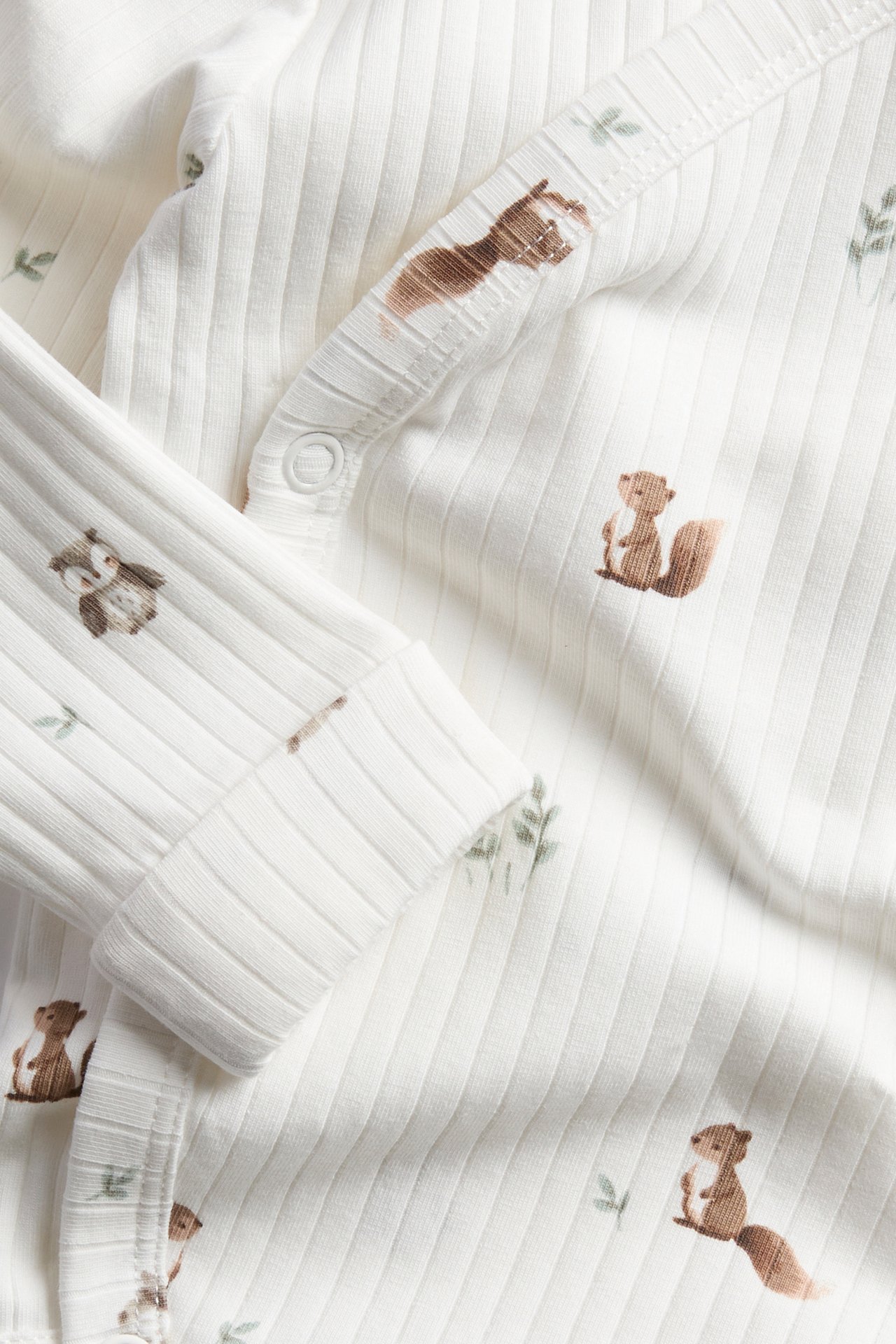 Nahaufnahme eines weißen gerippten Babybodys mit Eichhörnchen- und Eulenmuster, mit Druckknöpfen.