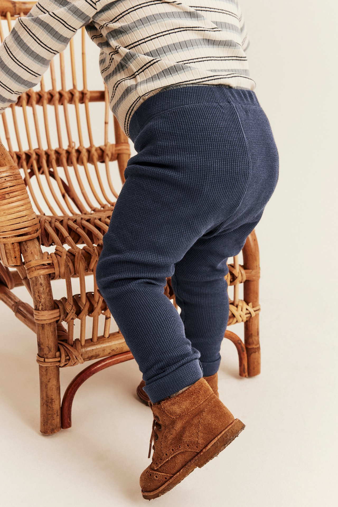 Seitenansicht Baby in marineblauen Waffelstrick-Leggings, gestreiftem Oberteil und braunen Wildlederstiefeln.