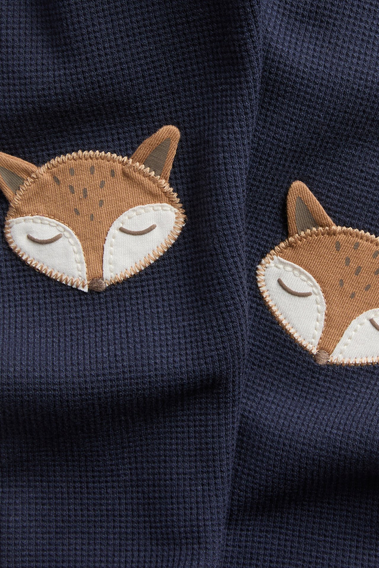 Close-up of navy blue waffle-knit fabric with two embroidered fox face appliques.
