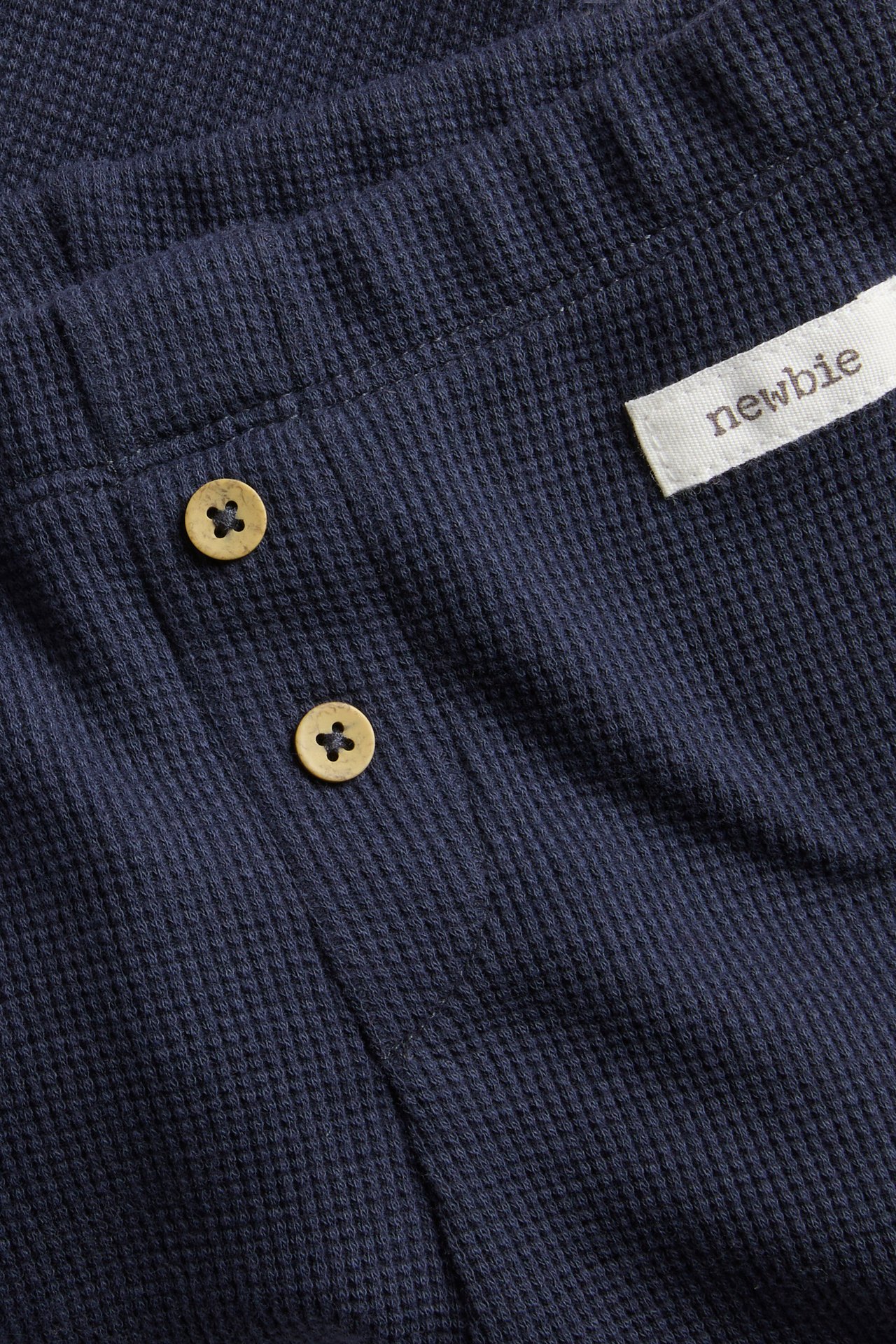 Close-up of dark blue waffle-knit fabric with two wooden buttons and a white woven label.