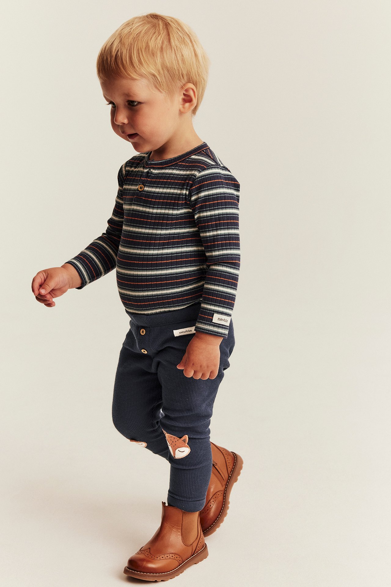 Seitenansicht Kind in gestreiftem Rippen-Langarmshirt, dunkelblauer Rippen-Leggings mit Fuchspatches und braunen Stiefeln.