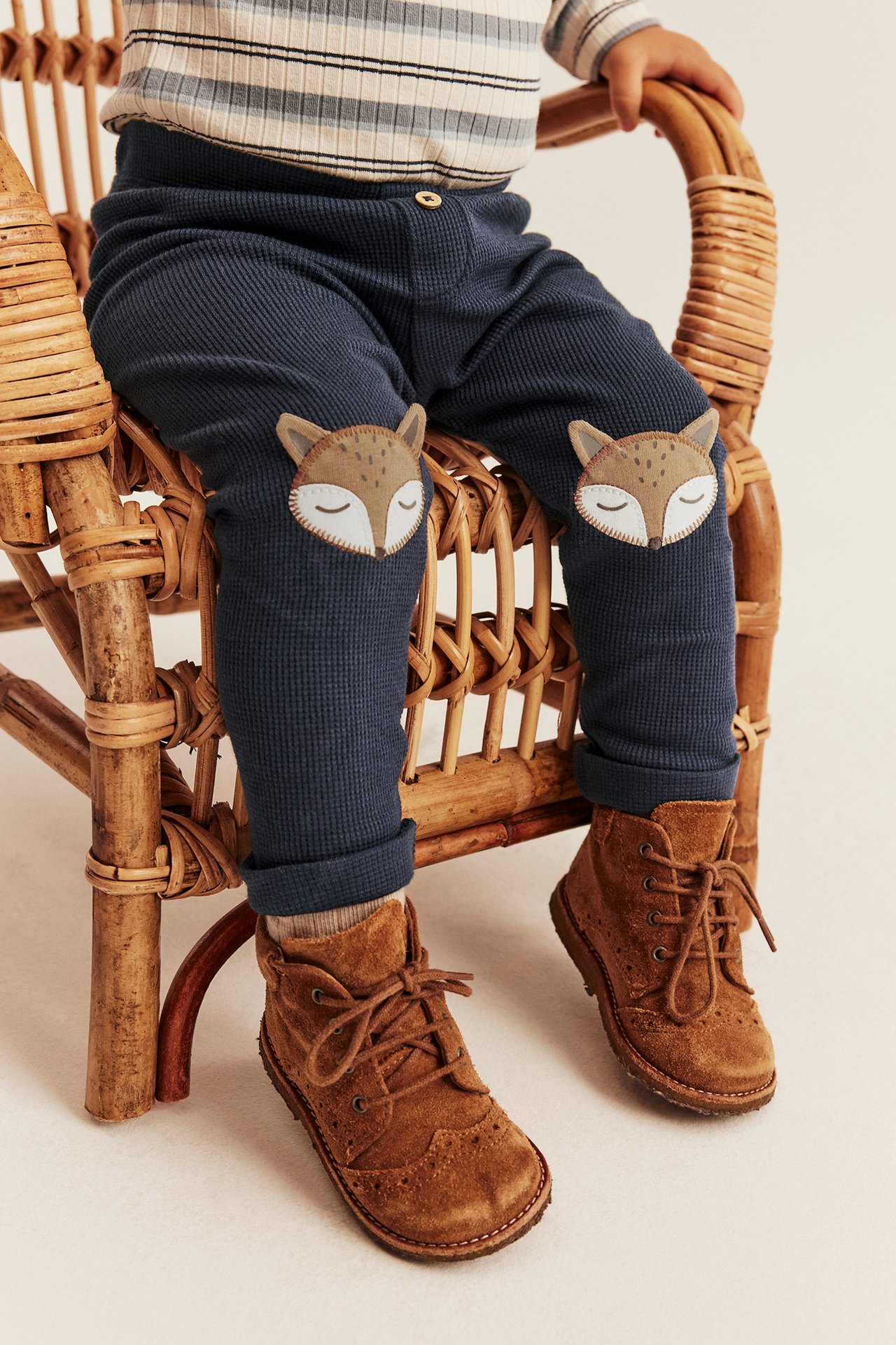 Baby trägt marineblaue gerippte Leggings mit Fuchsknie, gestreiftes Oberteil und braune Schnürboots.