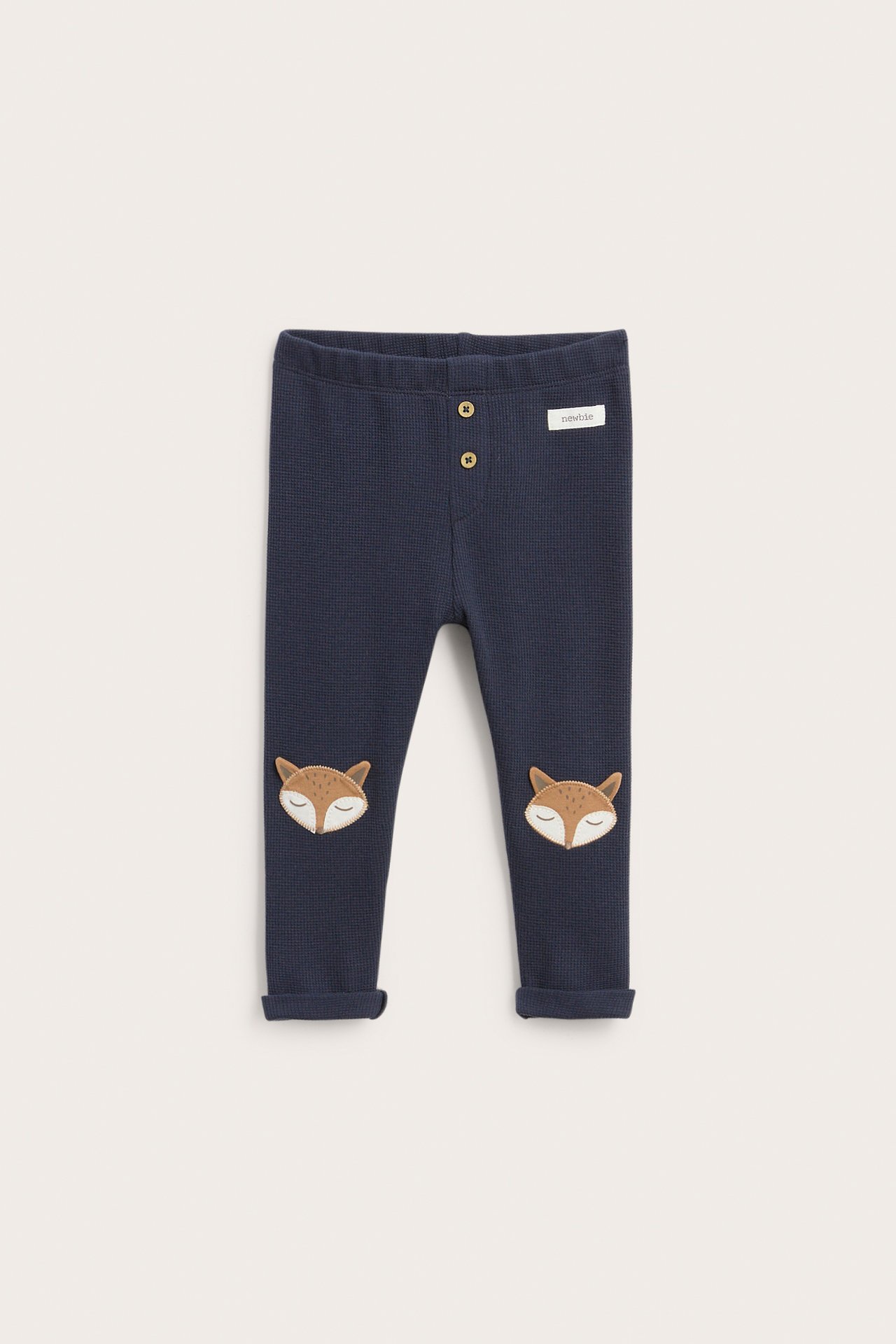 Front view of dark blue waffle knit baby leggings with fox patches, cuffed ankles, and front buttons.
