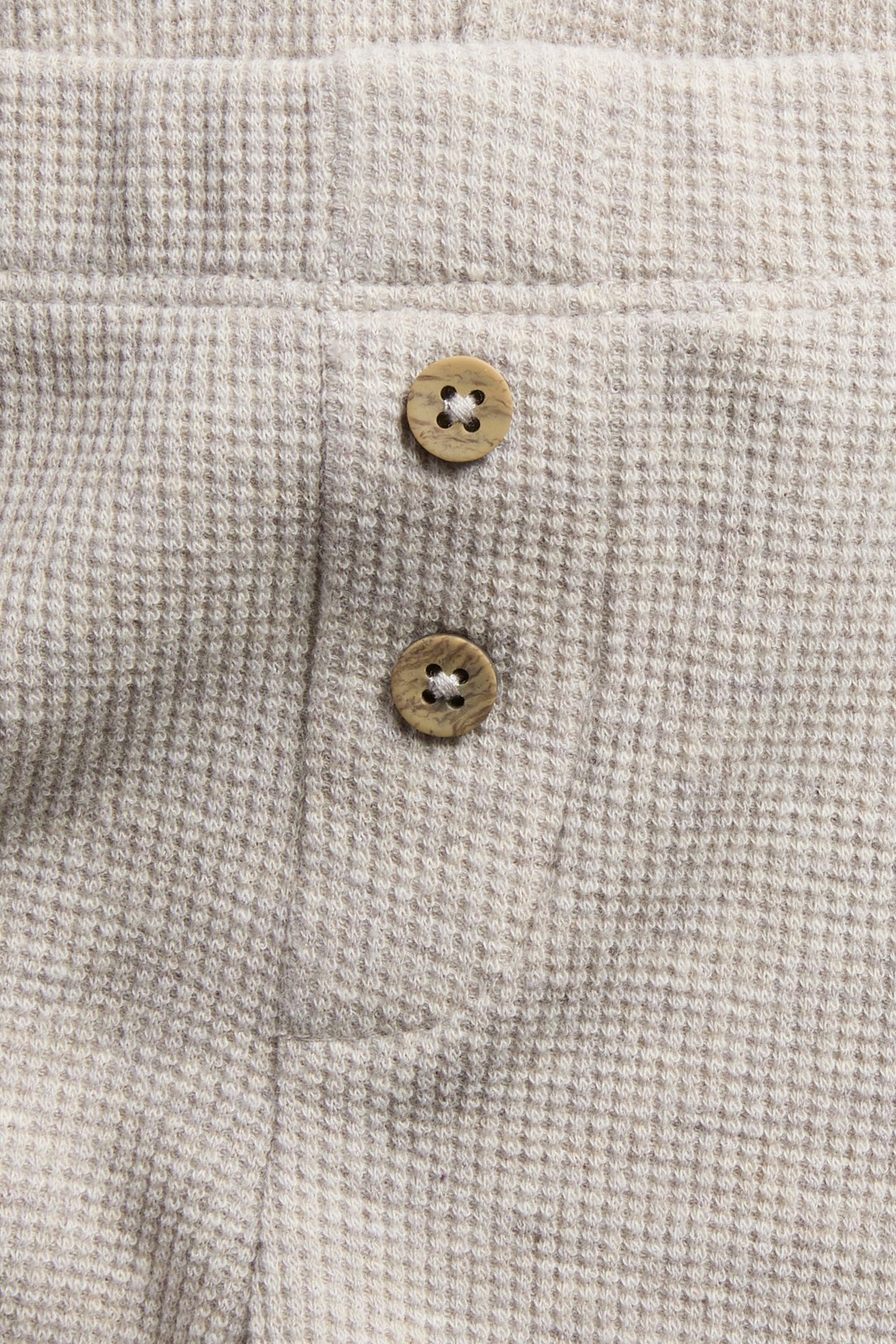 Close-up of light beige waffle knit fabric with two brown buttons.
