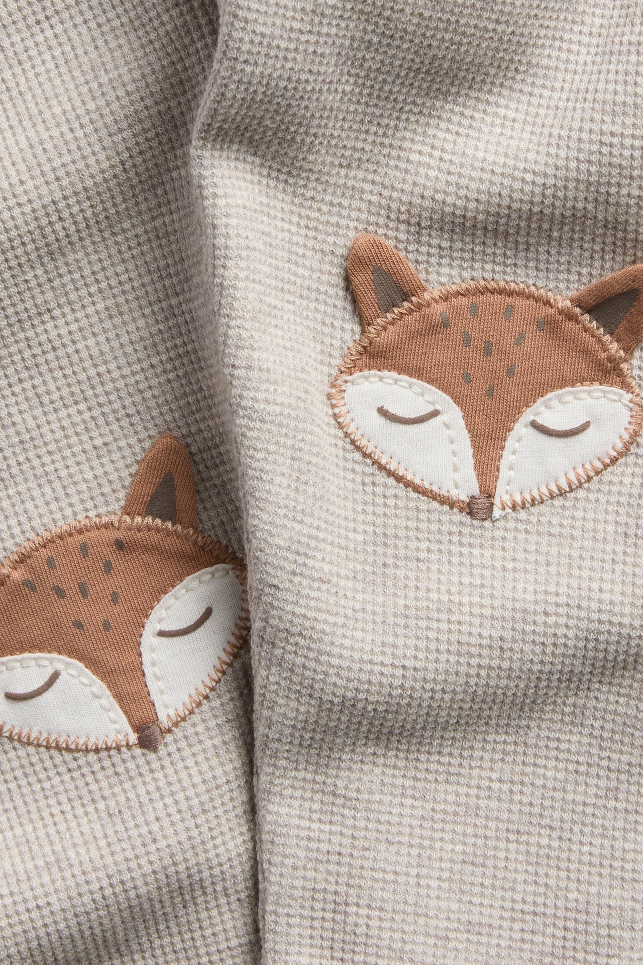 Nahaufnahme von hellbeigem Waffelstrickstoff mit zwei gestickten braunen Fuchsgesichtern.