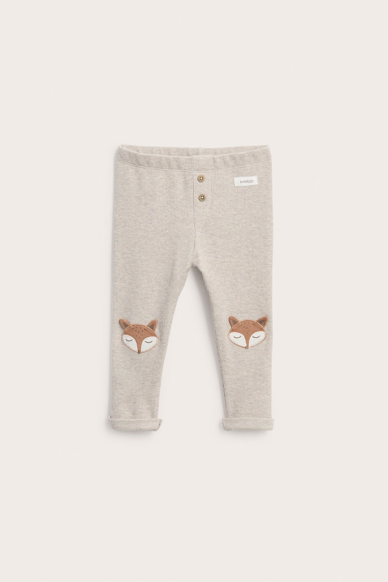 Vorderansicht von hellbeiger gerippter Babyhose mit zwei Knöpfen und Fuchskopf-Knieapplikationen.