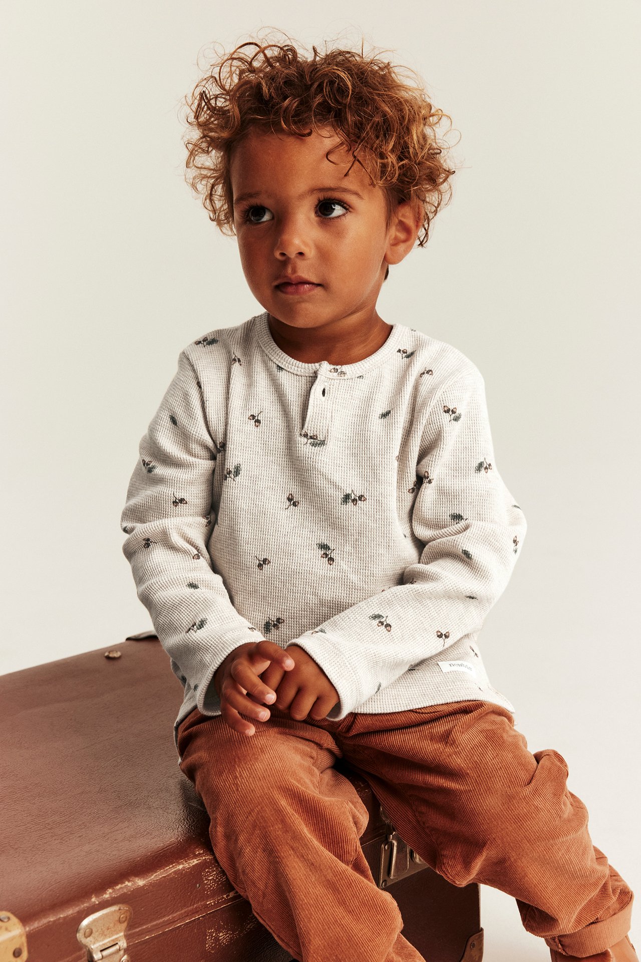 Front view of kid wearing a light beige waffle-knit long-sleeve top with berry pattern and rust corduroy pants.