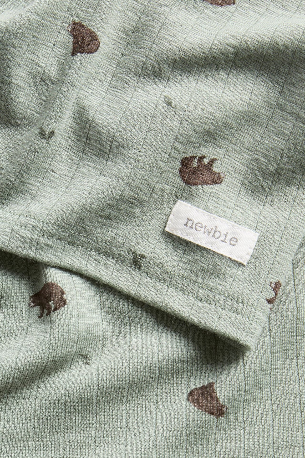 Close-up of a light green ribbed baby garment with brown bear print and 'newbie' label.
