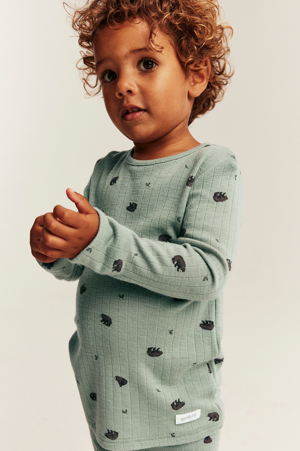 Front view of kid in light green ribbed long-sleeved top with bear print and matching pants.