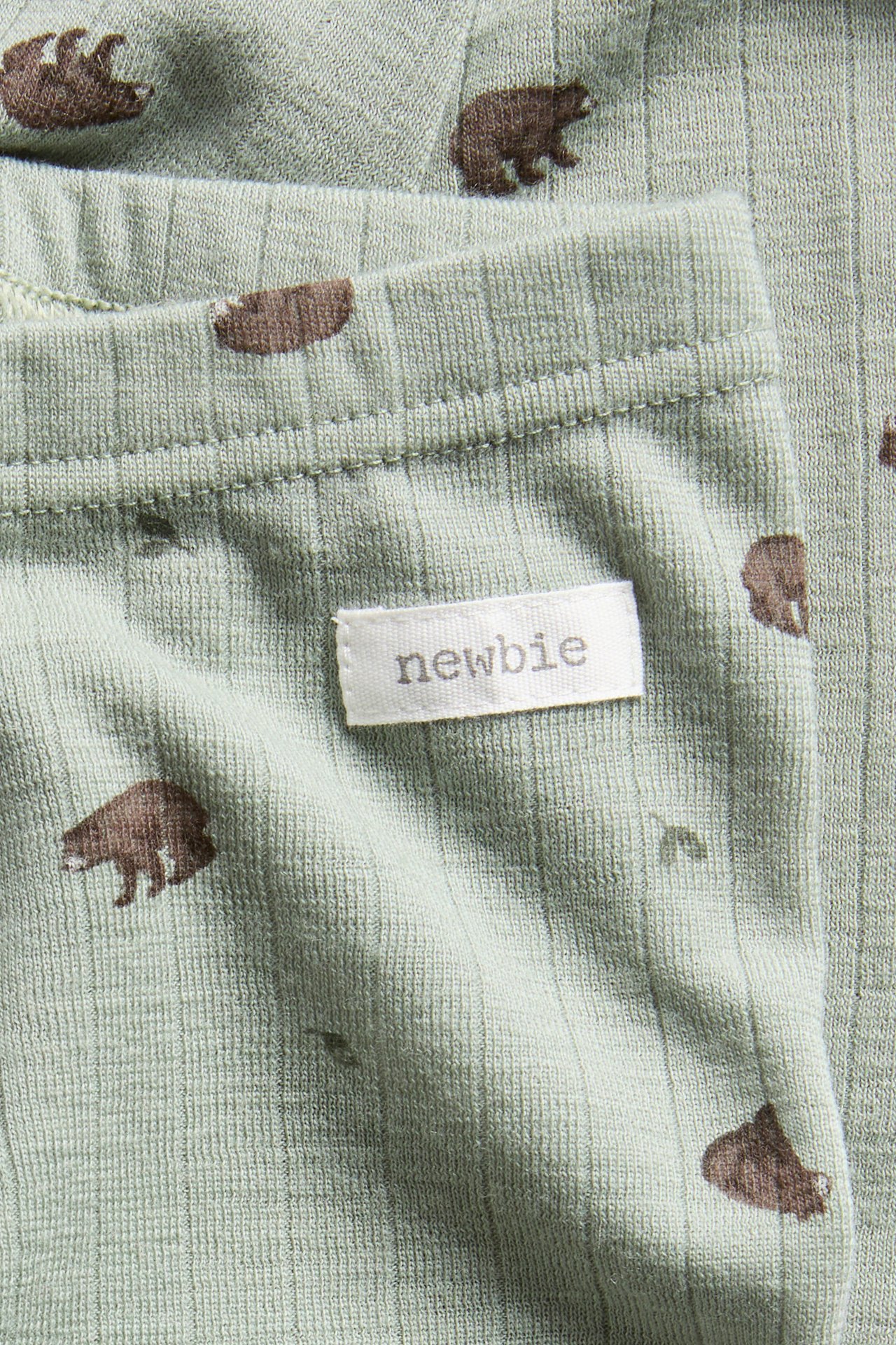 Nahaufnahme von hellgrüner gerippter Babykleidung mit braunem Bärenmuster und weißem Etikett.