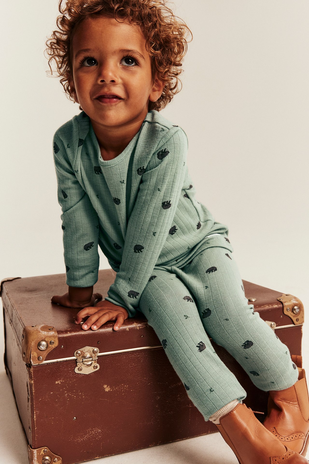 Front view of a kid in a ribbed sage green bear-pattern set with long-sleeve top, leggings, brown boots.