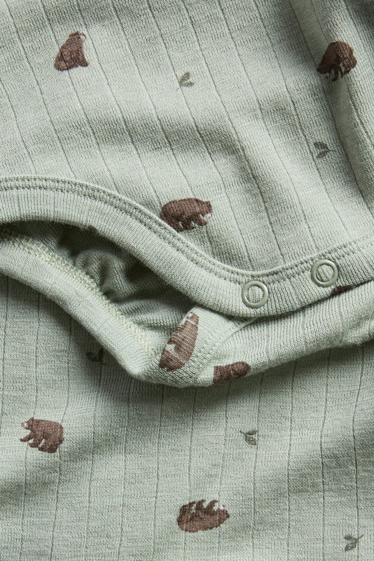 Close-up of a baby's light green ribbed bodysuit with brown bear print and two crotch snaps.