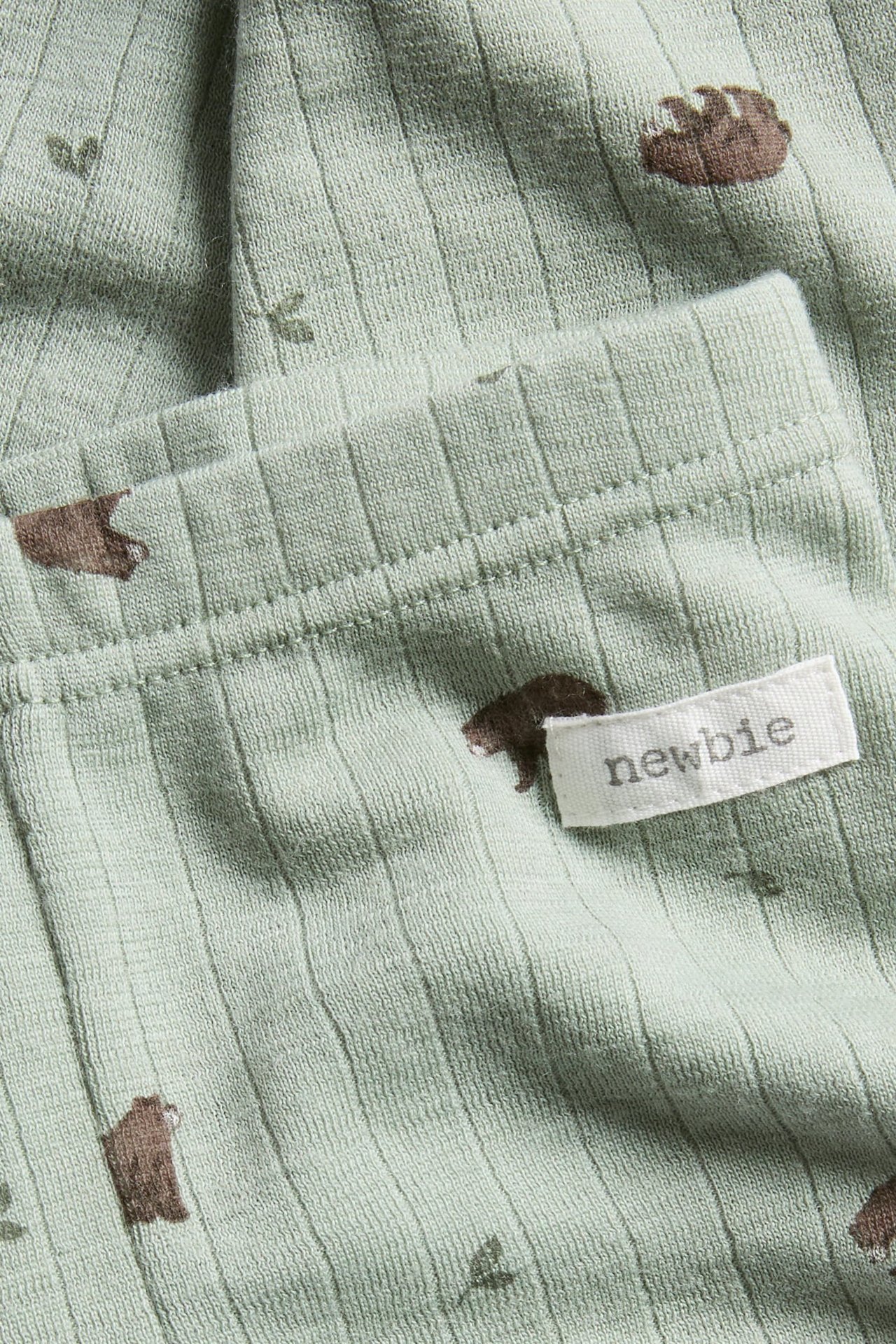 Close-up of baby's light green ribbed garment with bear and leaf print and 'newbie' label.