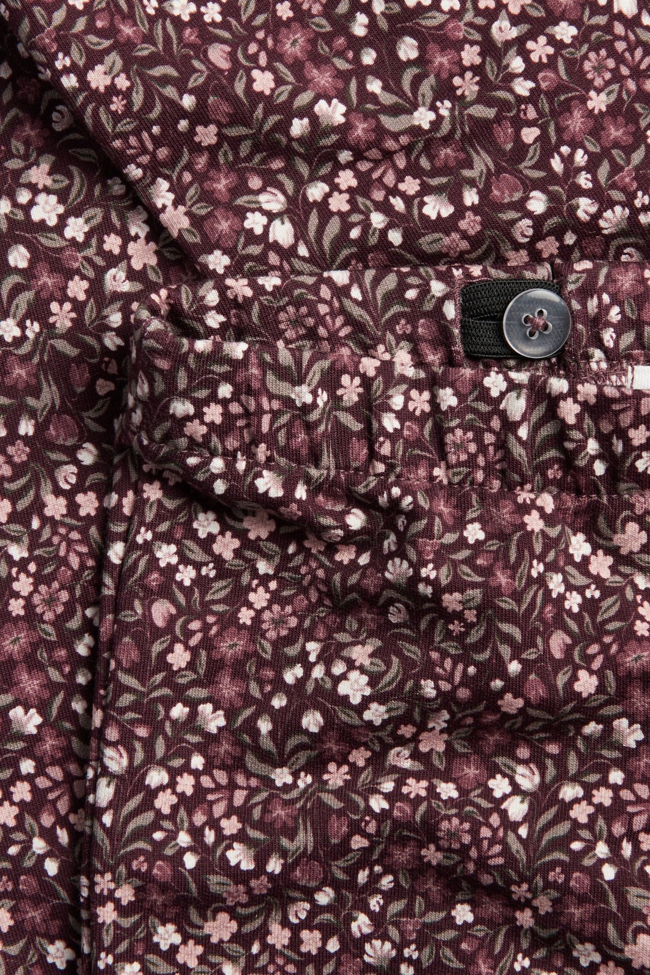 Nahaufnahme eines dunkelroten Kleidungsstücks mit kleinem Blumenmuster, elastischem Bund und verstellbarem Knopf.