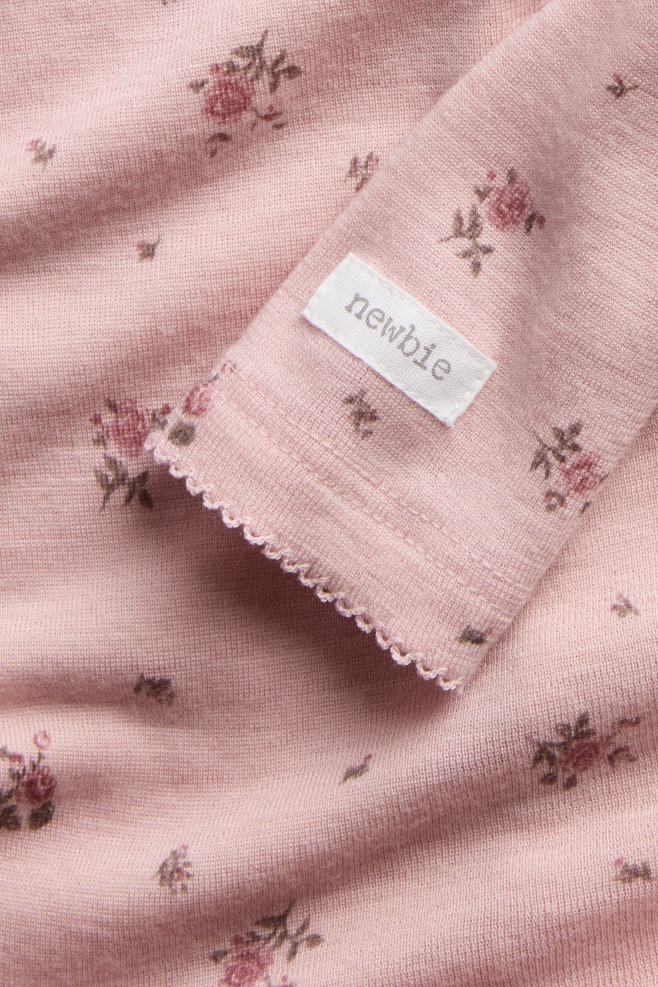 Close-up of a pink long-sleeved knit baby garment with a floral print and scalloped cuff.