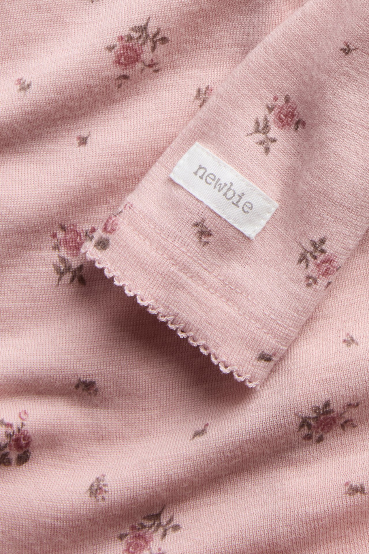 Nahaufnahme eines rosa langärmeligen Baby-Strickteils mit Blumenmuster und gewellter Manschette.