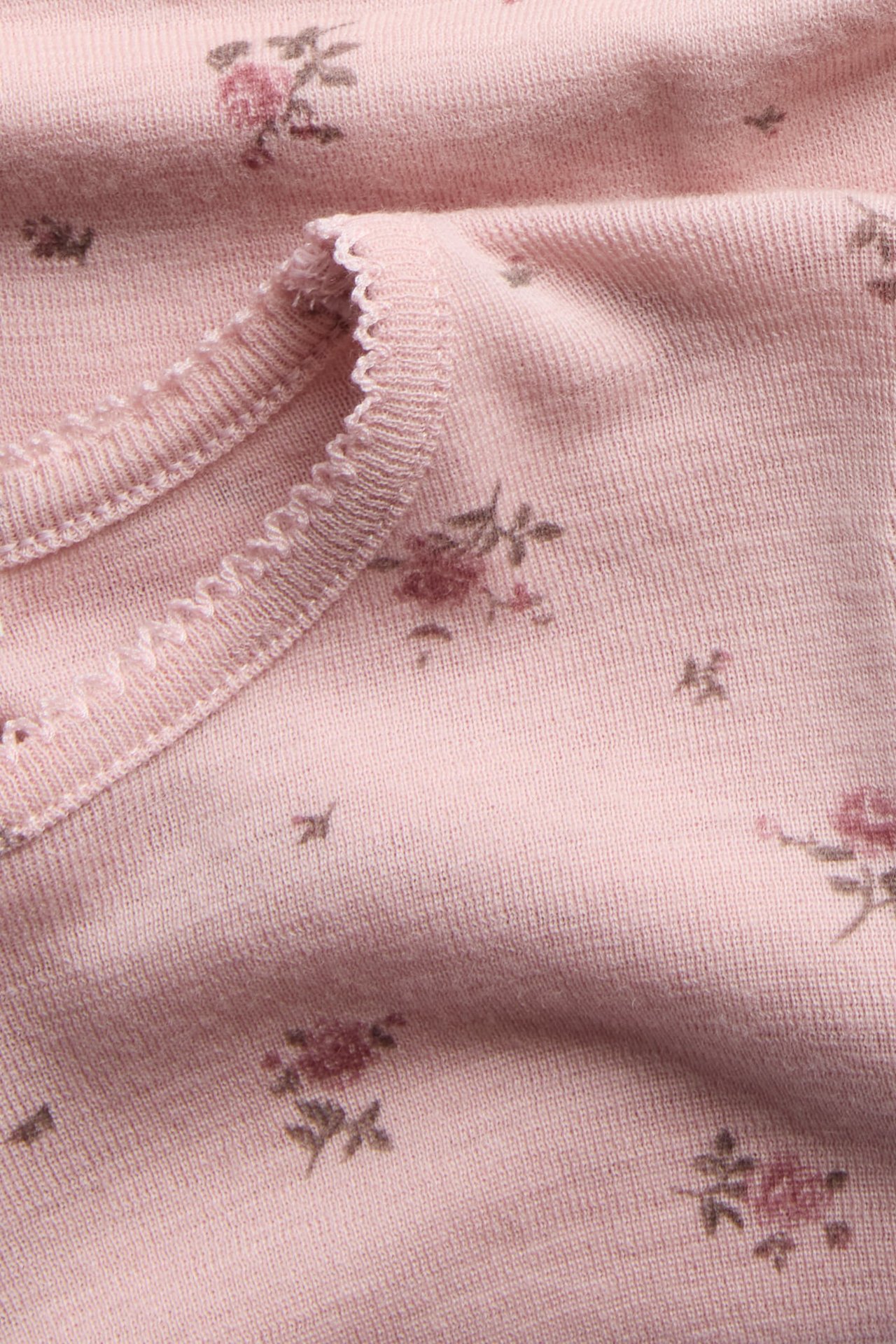 Close-up of a pink knit top with a delicate floral print and a ruffled trim.