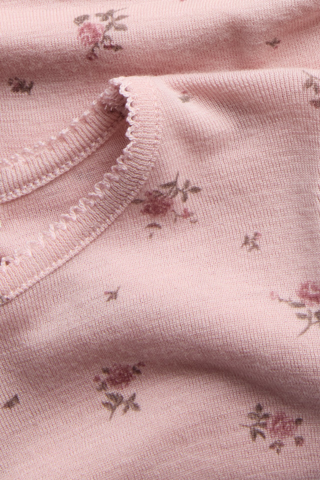 Nahaufnahme eines rosa Stricktops mit zartem Blumendruck und Rüschenbesatz.