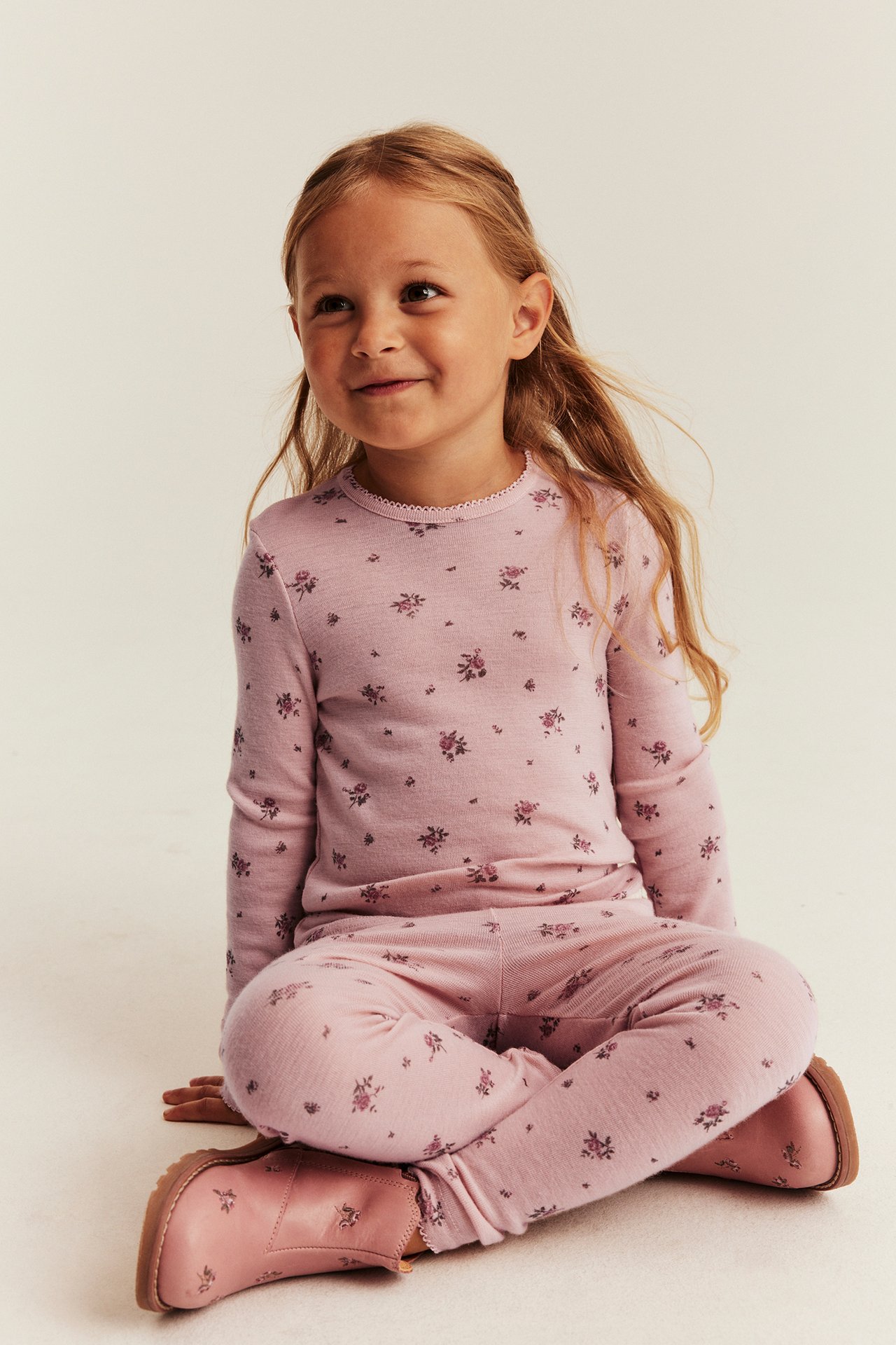 Vorderansicht: Kind in rosa geblümtem Ripp-Langarmshirt, Leggings und rosa Stiefeletten.